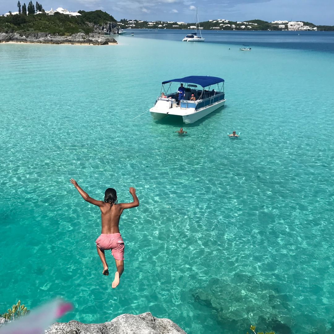 Person jumping from cliff into blue water, Castaway boat in background